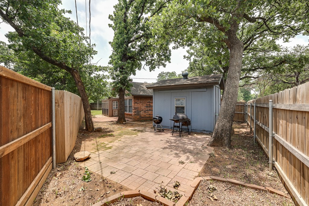 a backyard with a small blue shed and a fence and trees