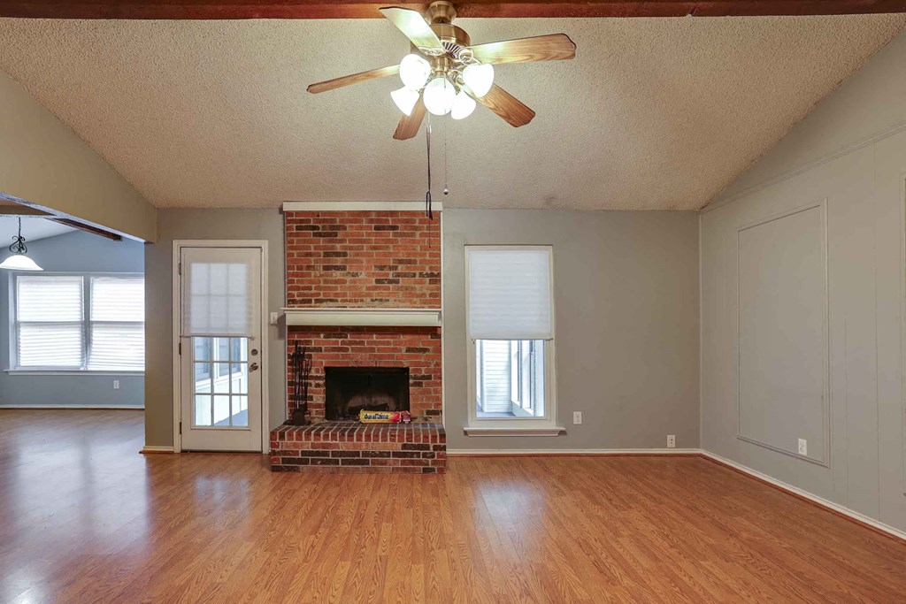an empty living room with a brick fireplace and a ceiling fan