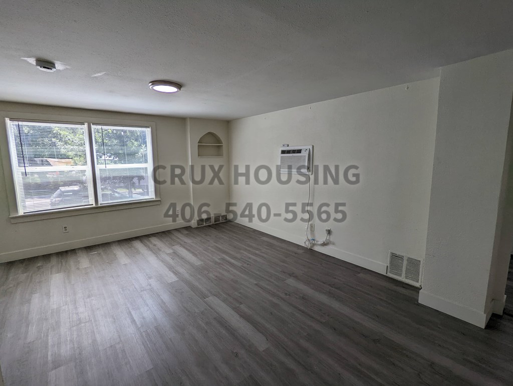 A room with wooden flooring and a window overlooking a parking lot.