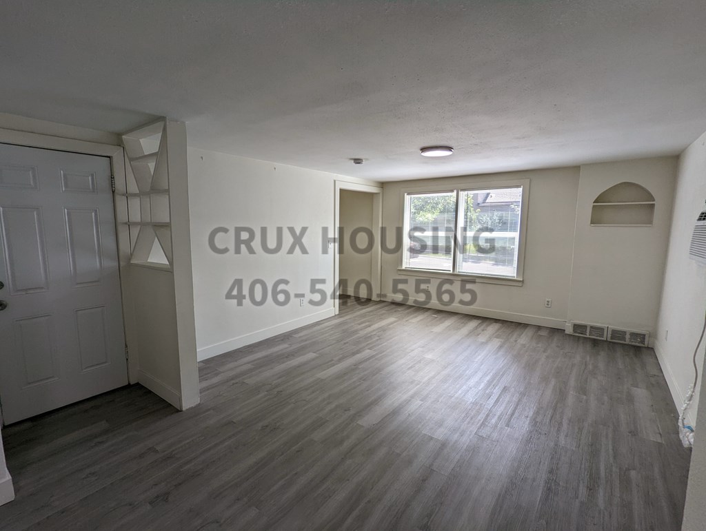 A room with wooden flooring and a white door, with the text "CRUX HOUSING" and a phone number on the wall.