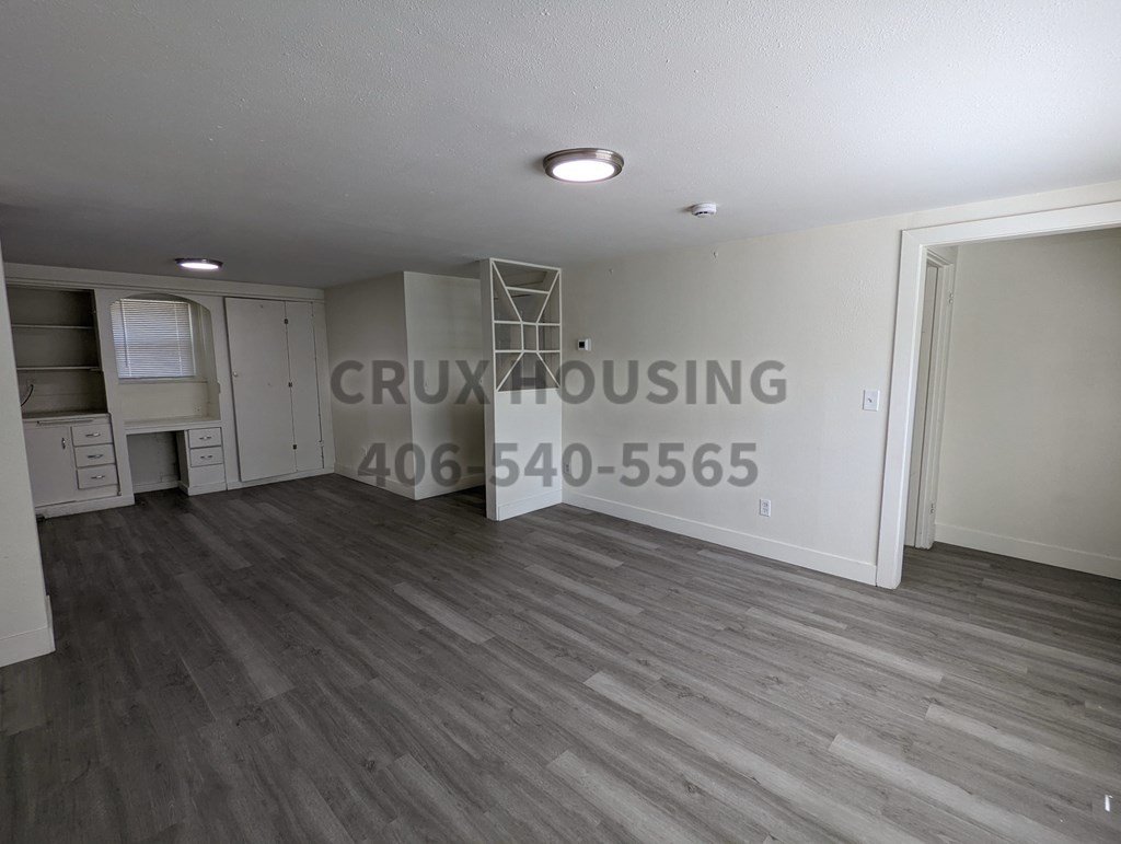 A room with wooden flooring and a white wall with the text "CRUX HOUSING" and a phone number.