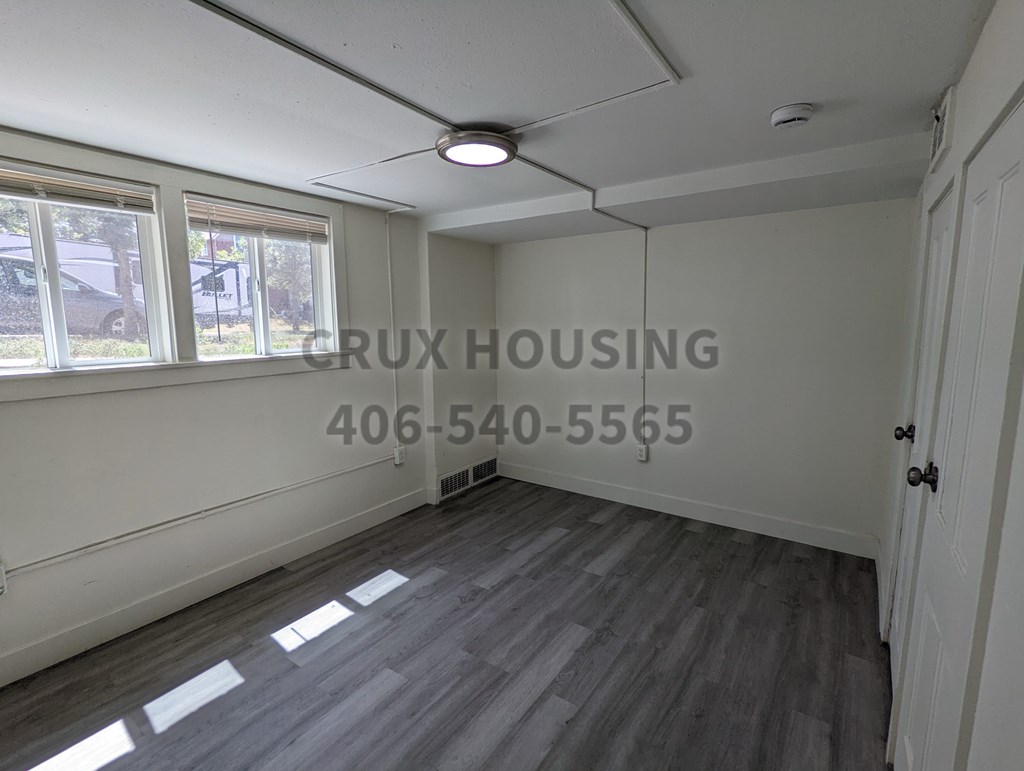 A room with a white ceiling and a window with a view of a car and trees outside.