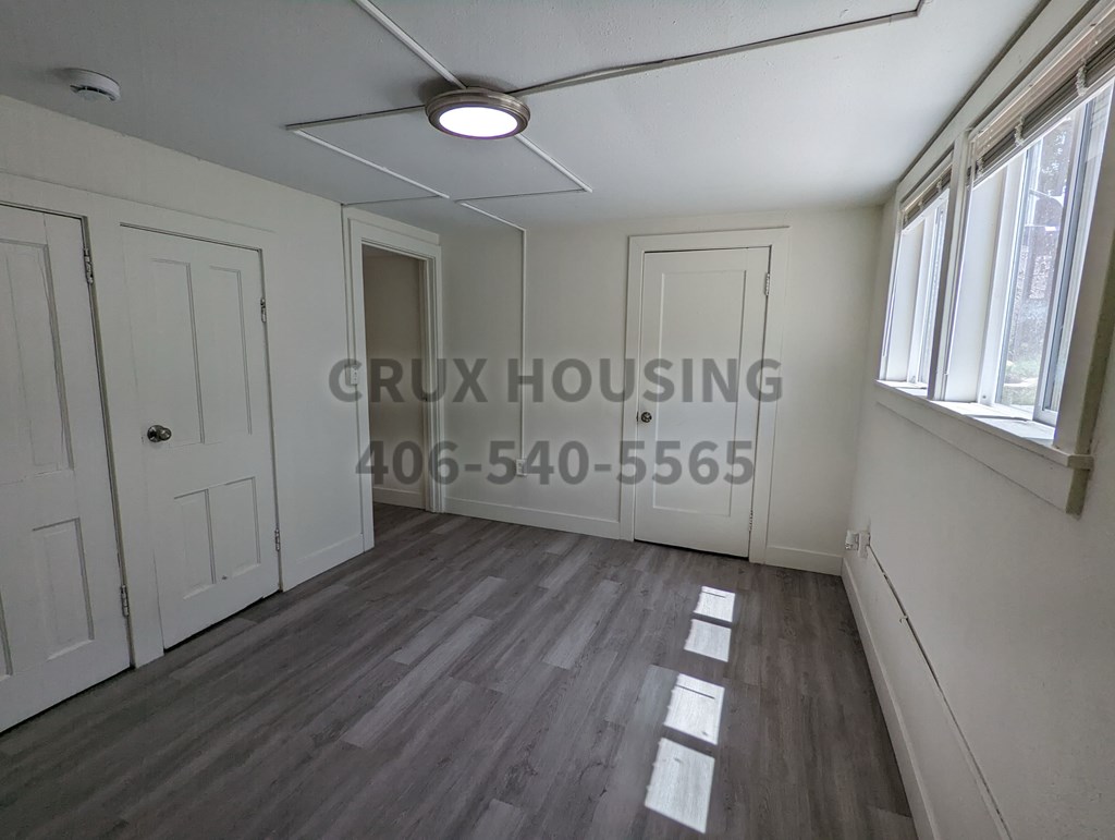 A room with a wooden floor and white walls, with a window on the right side.