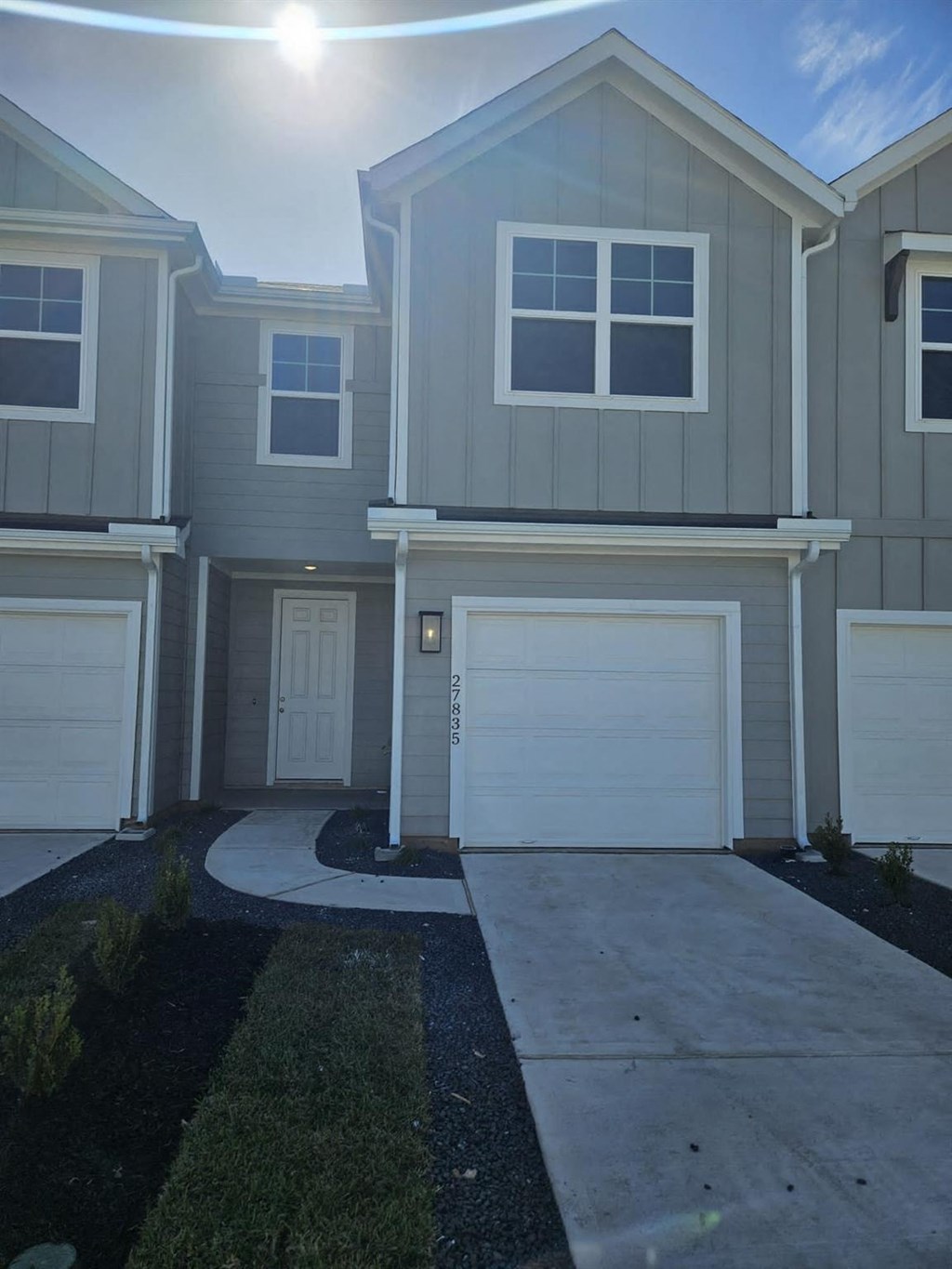 a sidewalk in front of a house with two garage doors