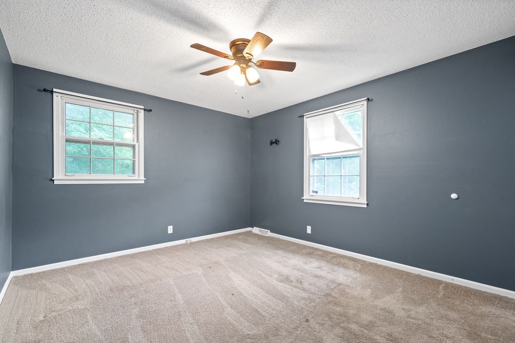 the bedroom is empty and has a ceiling fan and two windows