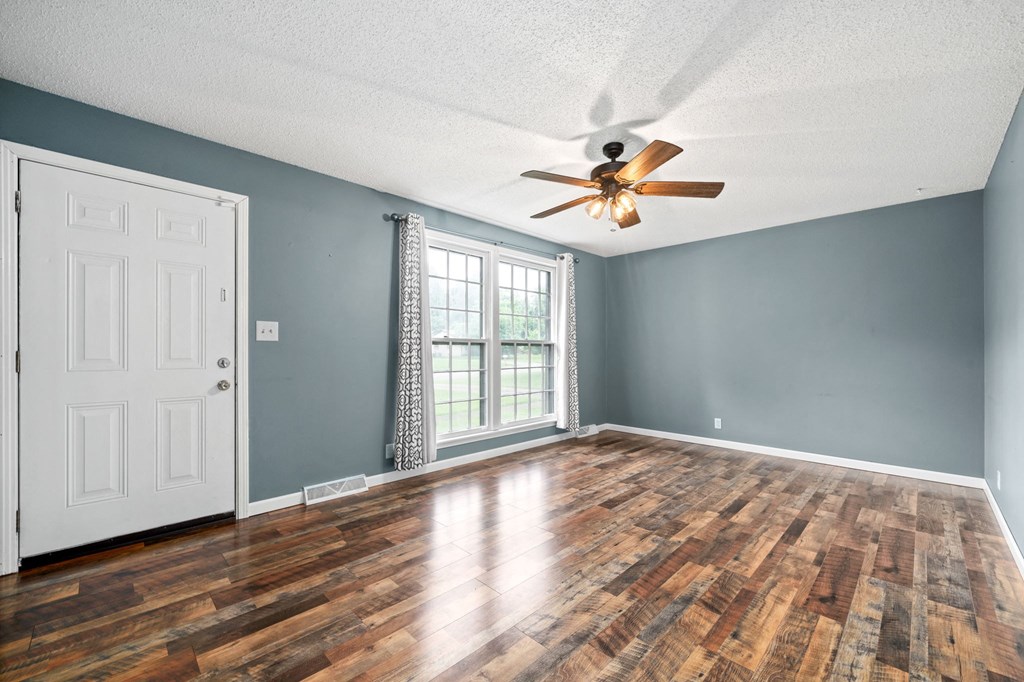 an empty living room with wood floors and a ceiling fan