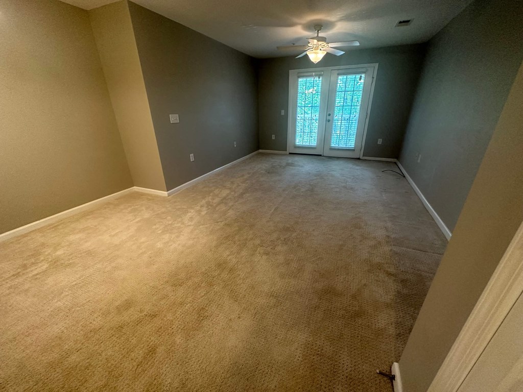 a empty living room with carpet and a ceiling fan