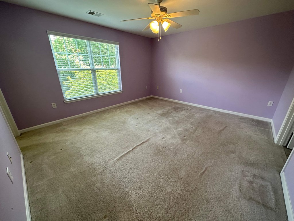 a empty bedroom with purple walls and a ceiling fan