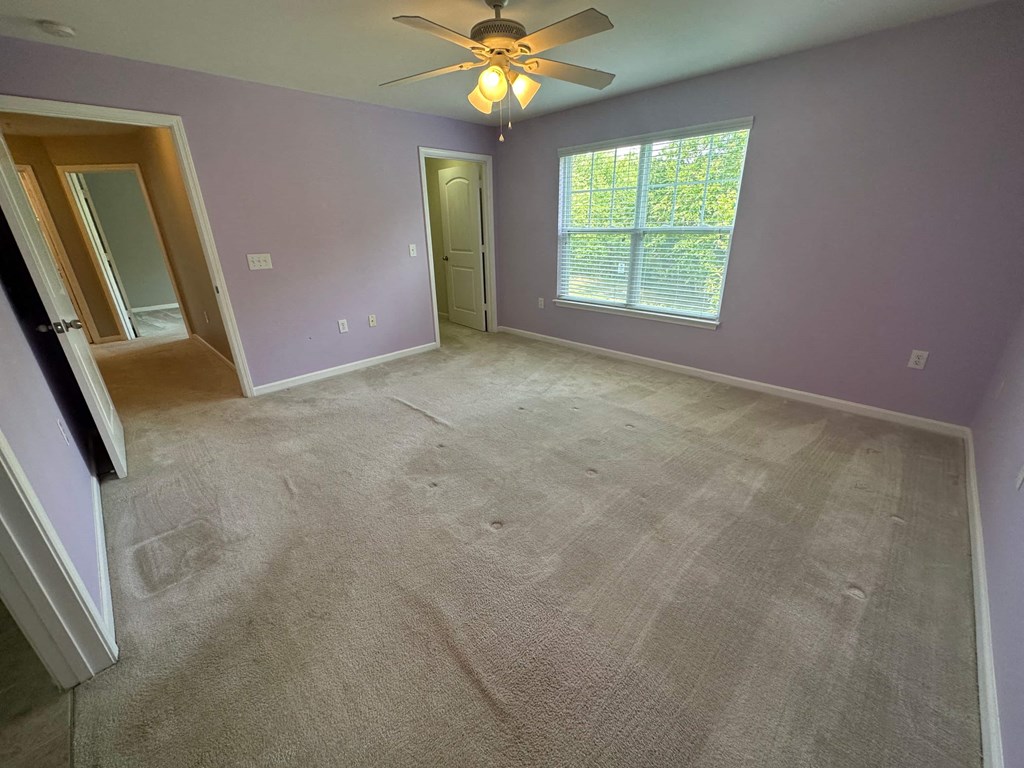 a empty living room with carpet and a ceiling fan
