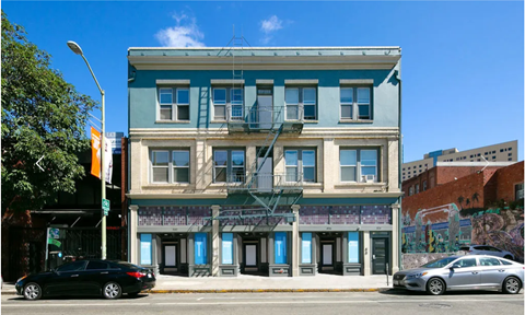 A black car is parked on the street in front of a blue building.