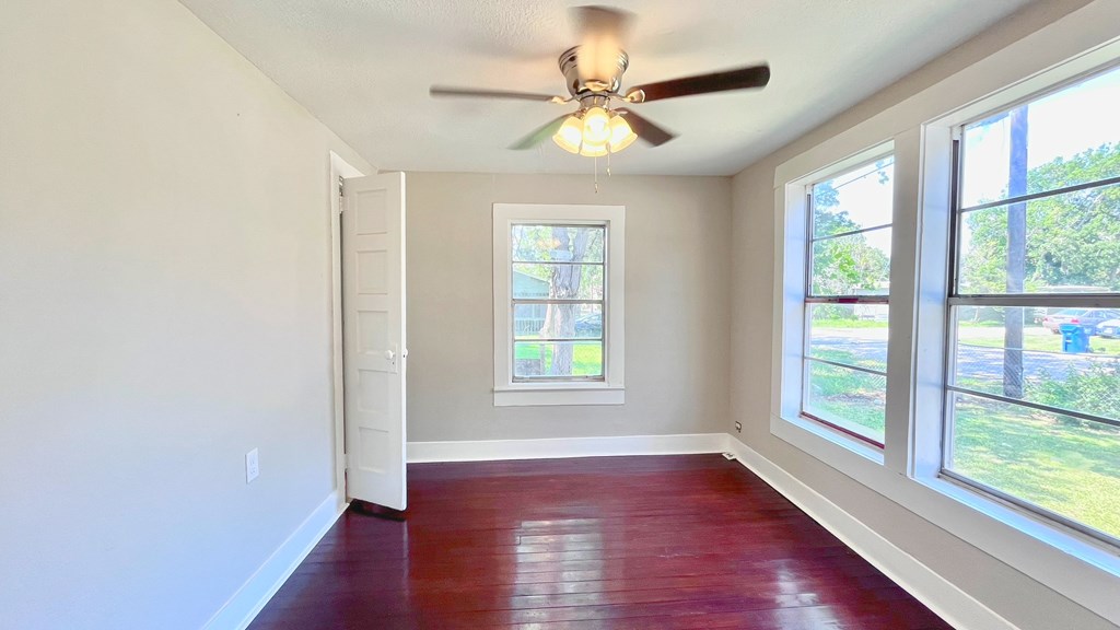 an empty living room with a ceiling fan and three windows