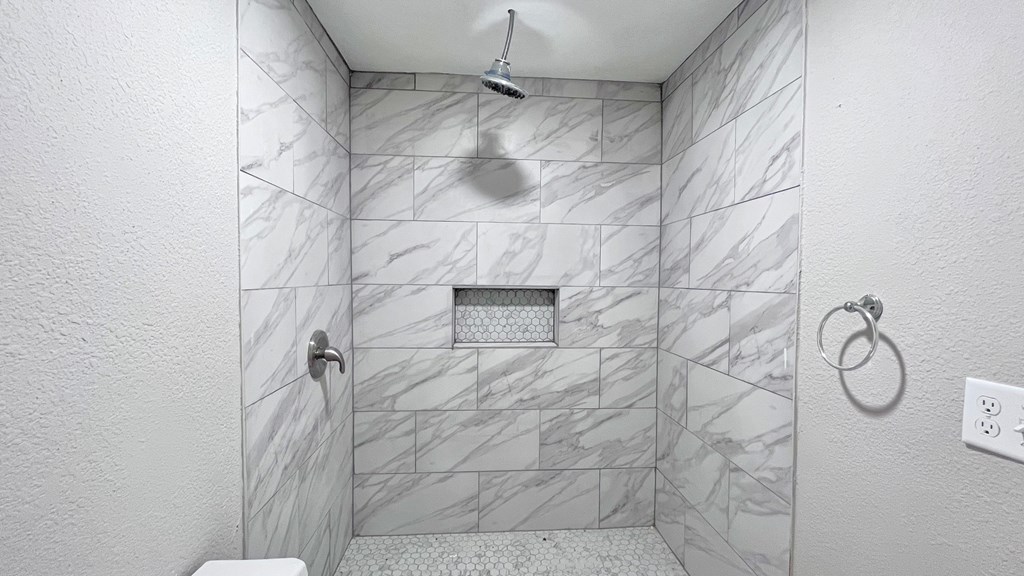 the shower is tiled in marble and has a rainfall shower head in it