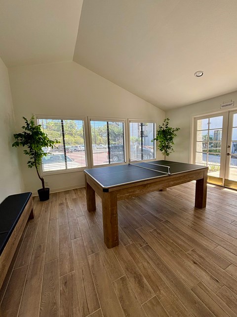 A ping pong table is in the middle of a room with wood flooring and a window.