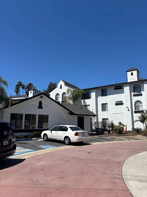 A white car is parked in a parking lot in front of a white building.