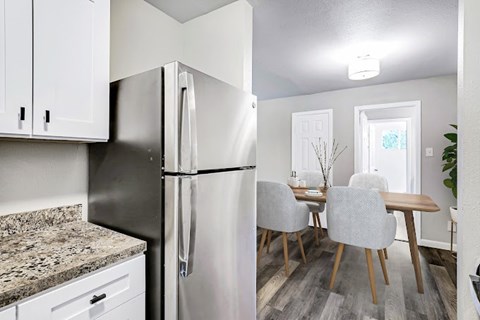 A kitchen with a refrigerator, cabinets, and a dining table.