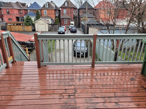 A wooden deck with a metal railing and a car parked in the background.