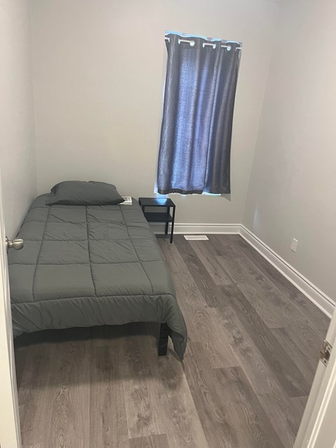 A bedroom with a bed, nightstand, and window with curtains.