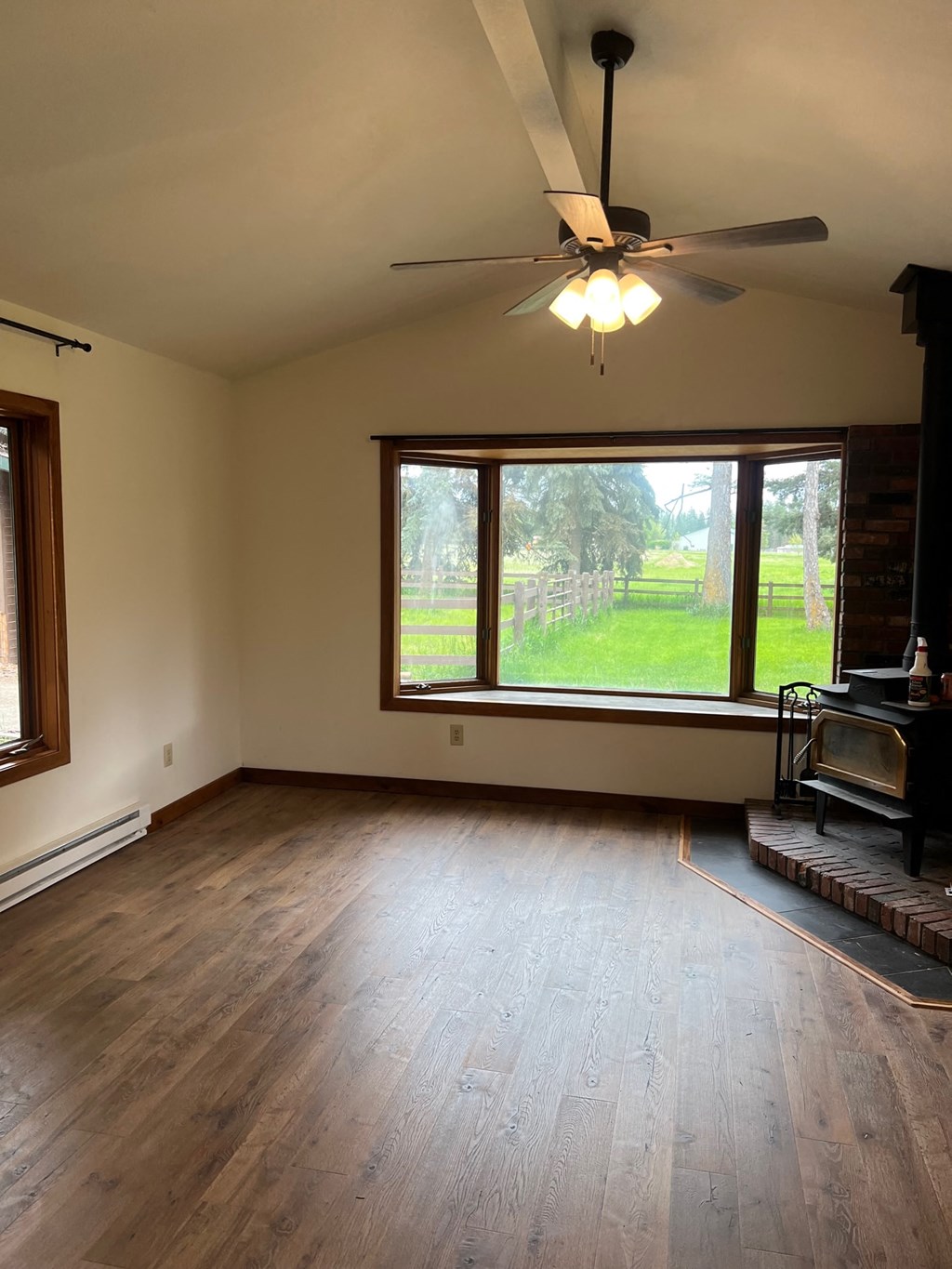 an empty living room with a large window and a ceiling fan