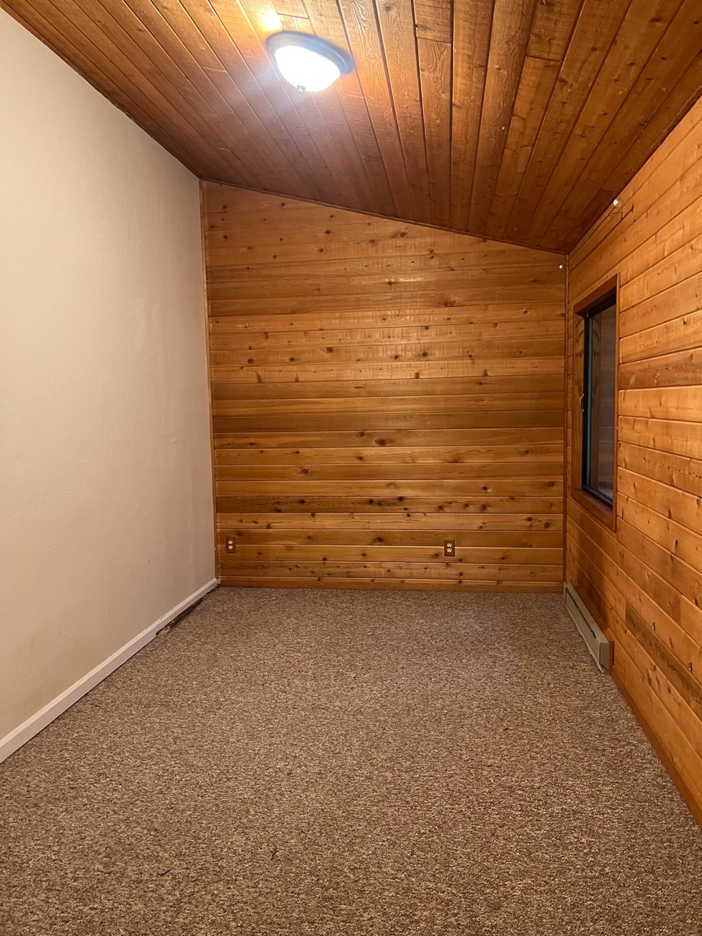 the upstairs bedroom has a wood paneled wall and carpeted floor