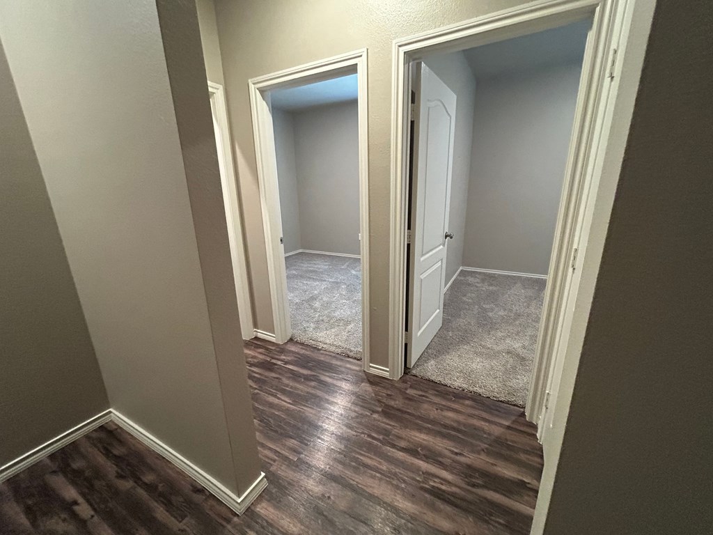 A hallway with a carpeted floor and two open doors.