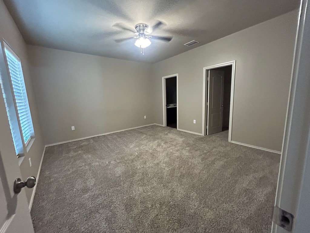 A room with a carpeted floor and a ceiling fan.