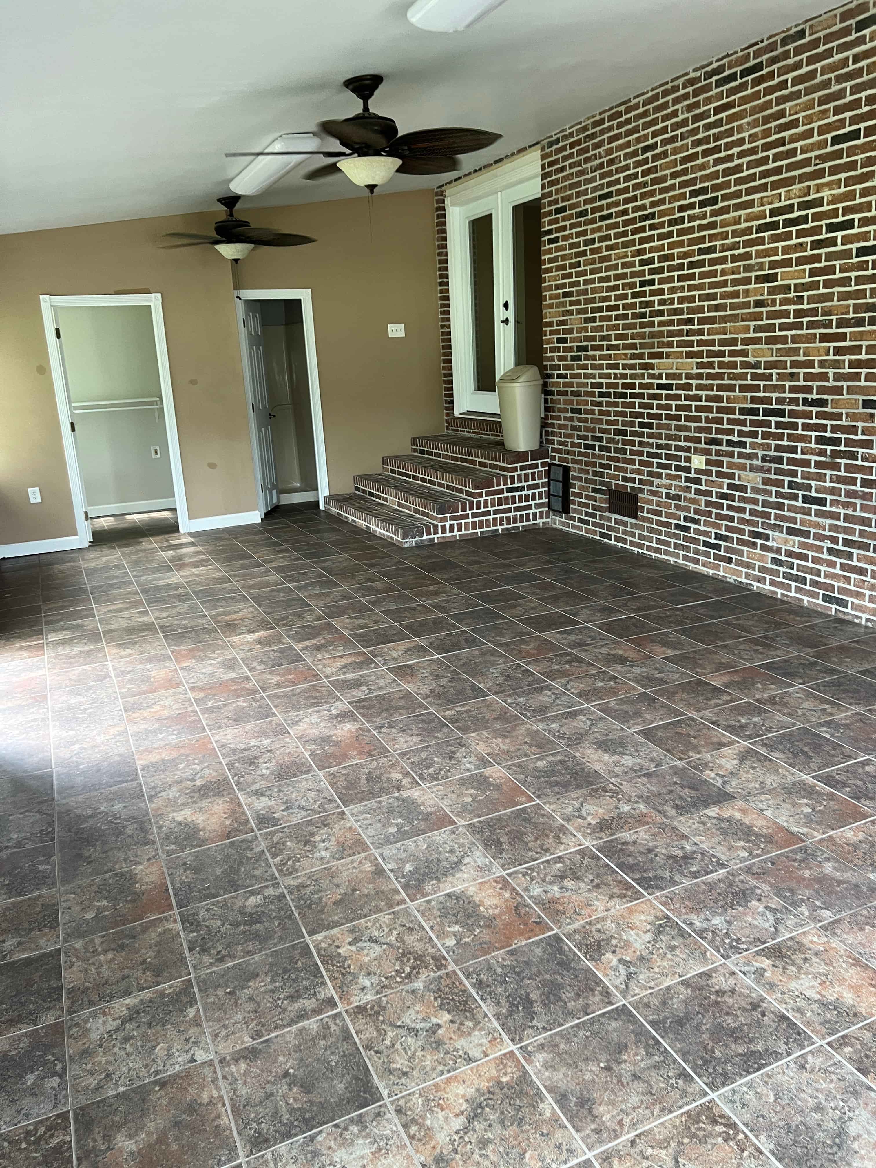 an empty living room with tile flooring and a brick wall