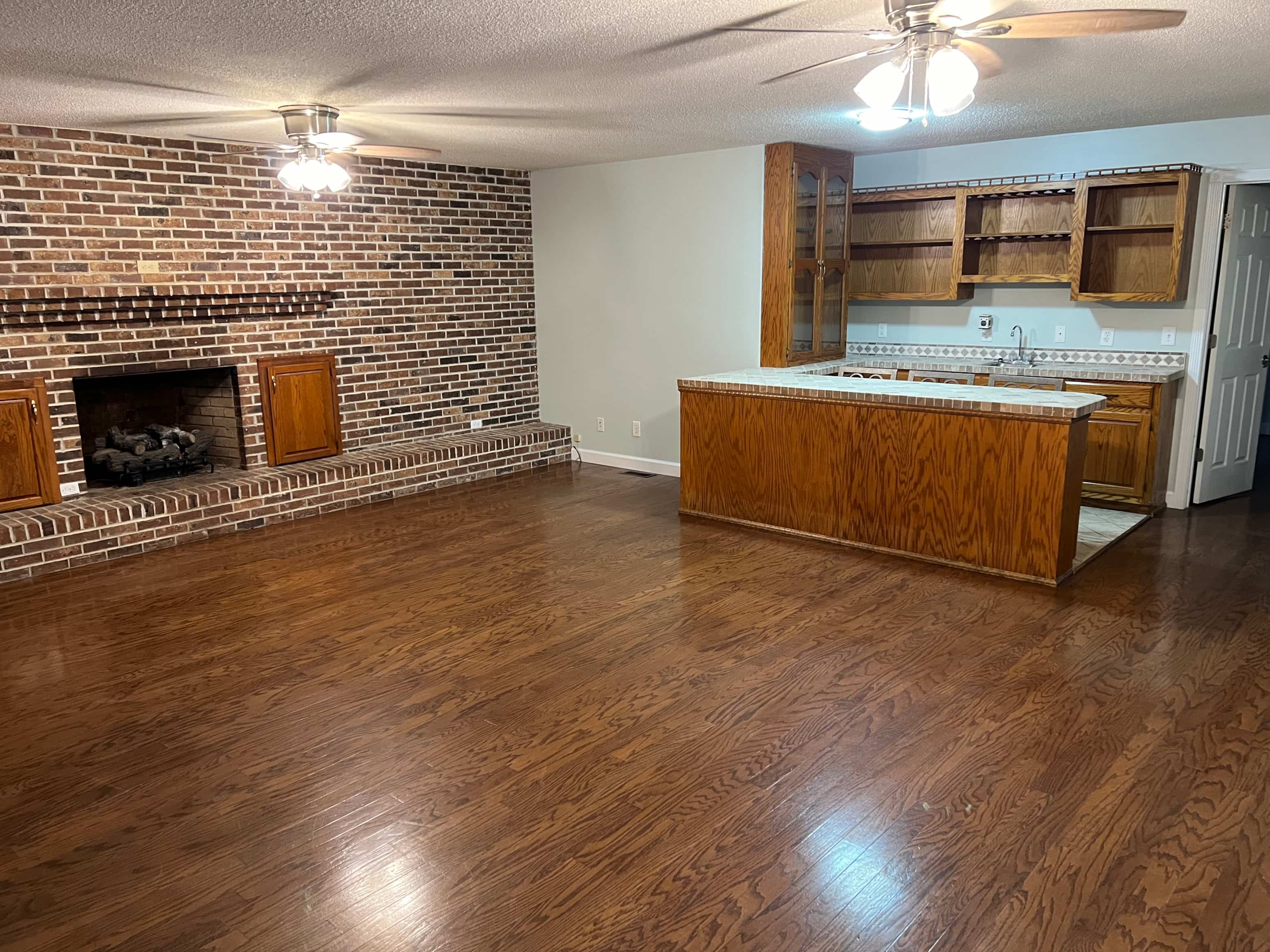 an empty living room with a brick fireplace and a kitchen