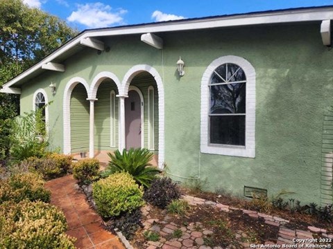 the front of a green house with a brick walkway