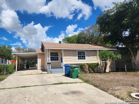a small tan house with a driveway and a trash can