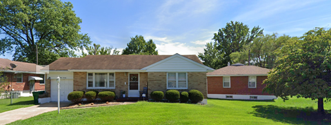 a small brick house with a lawn and trees