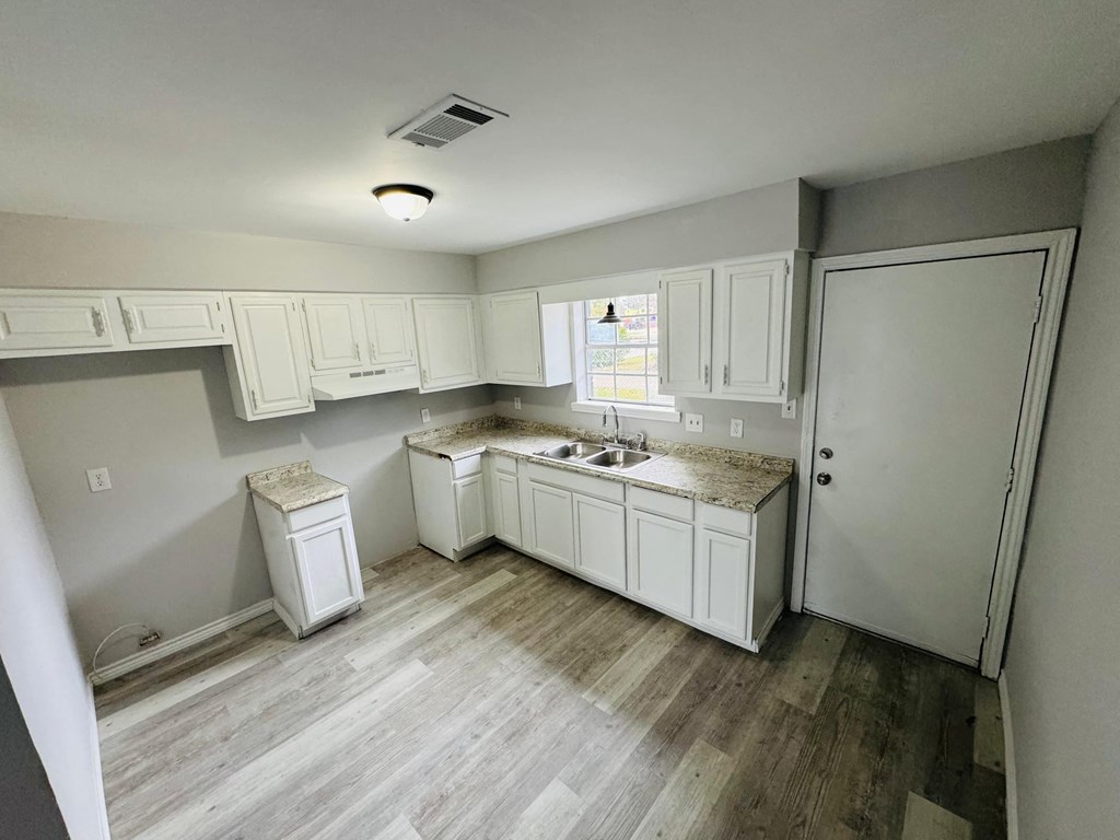a remodeled kitchen with white cabinets and wood floors