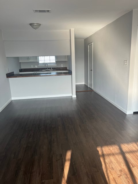 an empty living room with wood floors and a kitchen