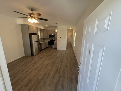 an empty living room and kitchen with wood flooring and a ceiling fan