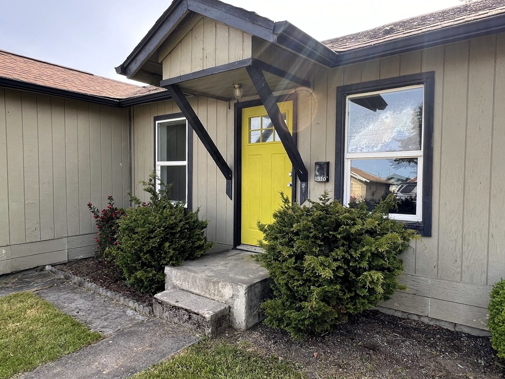 the front door of a yellow house with a porch