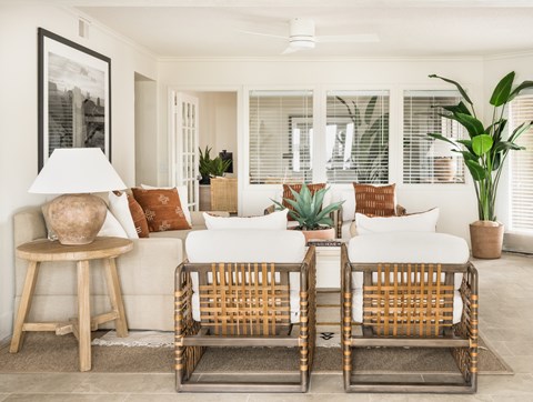A living room with a white couch, two chairs, and a table with a lamp and vase.