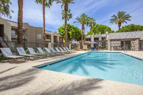 A swimming pool surrounded by palm trees and lounge chairs.