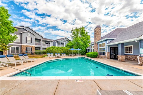 A swimming pool in front of a building with a blue sky and clouds in the background.