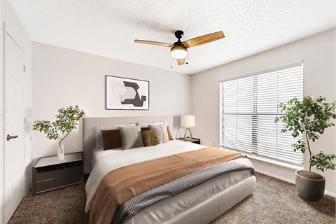 A bedroom with a bed, a ceiling fan, and two potted plants.