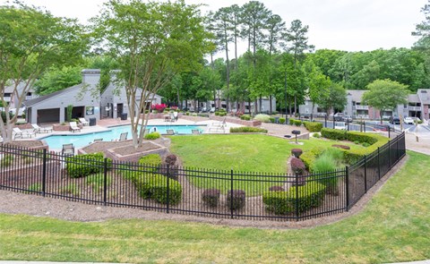 A black fence surrounds a green lawn and a pool.
