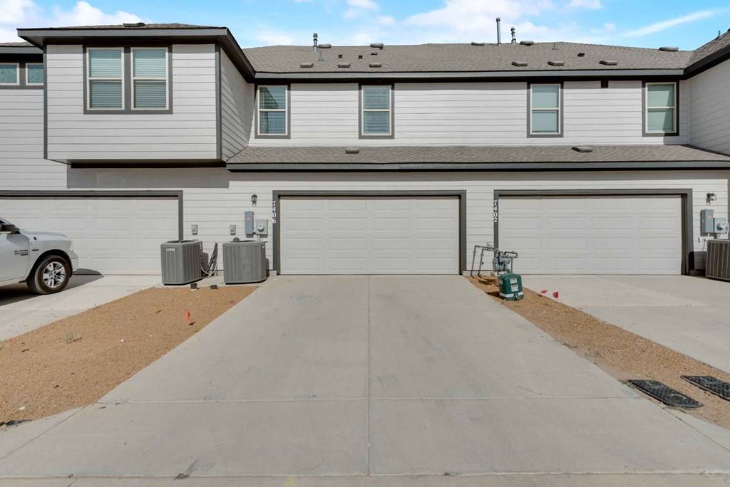the front of a white house with a driveway and garage doors