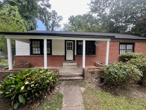 a small brick house with white pillars and a porch