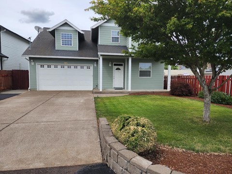 a green house with a driveway and a tree