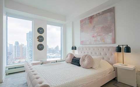 A bedroom with a large bed and a city view through the window.
