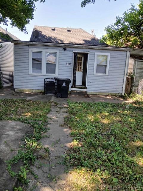 a small white house with a yard and a trash can