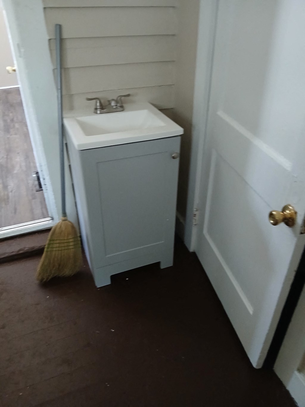 a bathroom with a sink and a broom next to a door