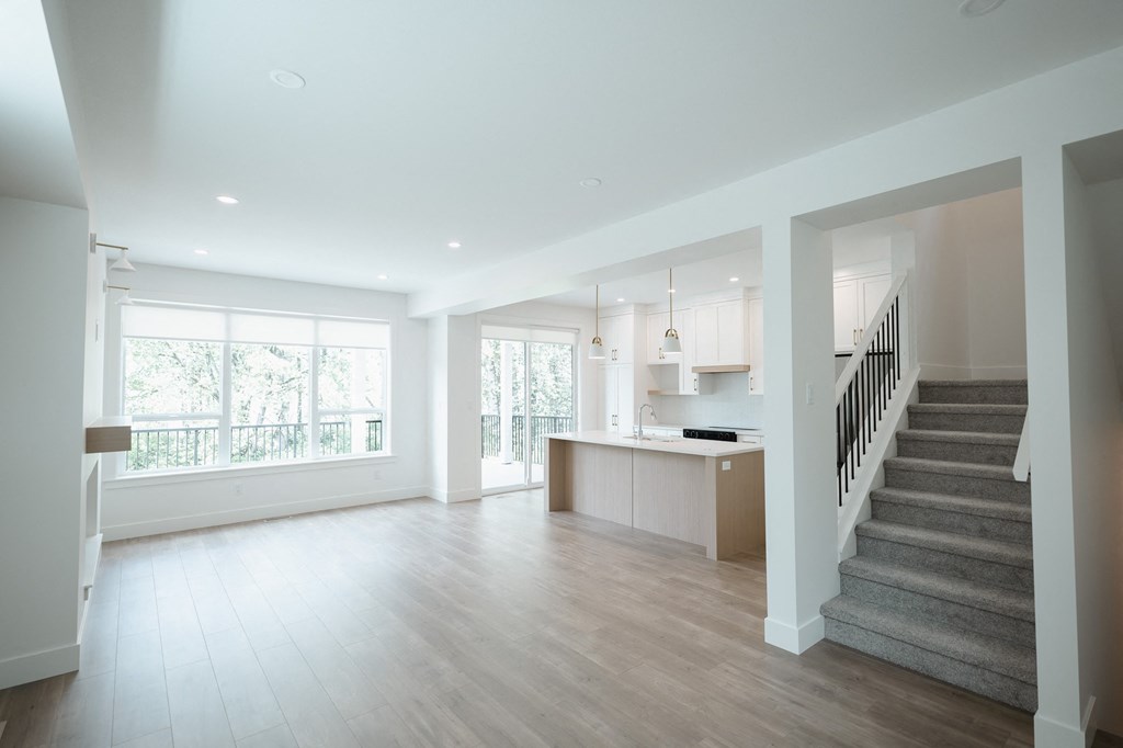 an empty living room with a staircase and a kitchen