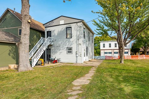 a white house with a sidewalk and a green house next to it