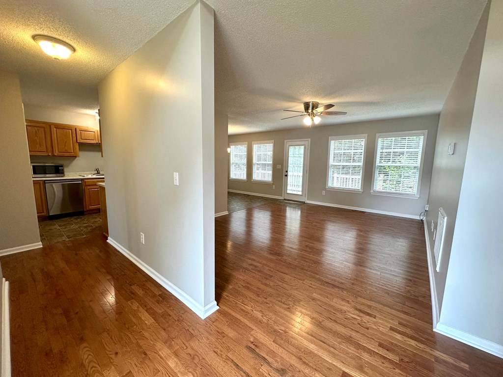 an empty living room and kitchen with wood floors and a ceiling fan