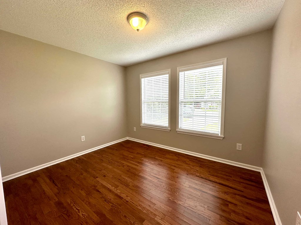 an empty living room with wood flooring and two windows