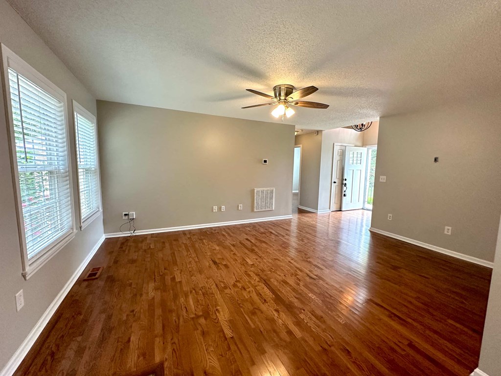 an empty living room with wood floors and a ceiling fan